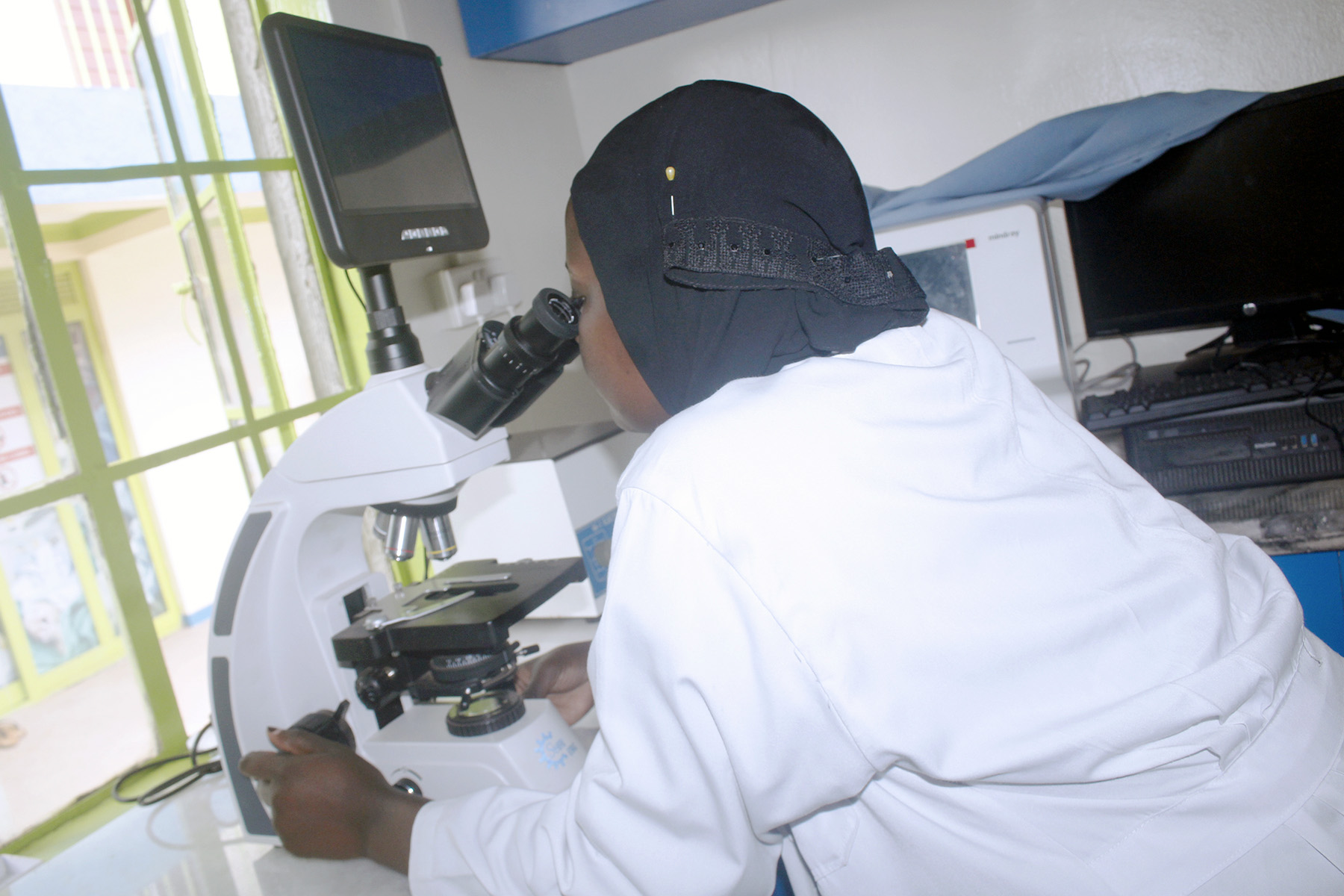 Laboratory technician examining samples under a microscope at Family Clinic